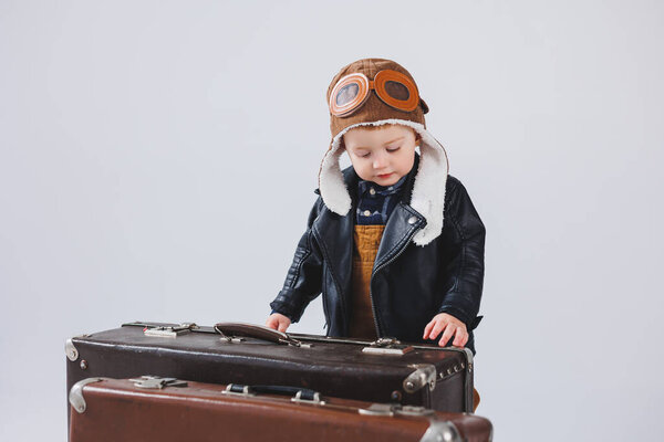 Happy little boy with a brown suitcase. Portrait of a child tourist, a child in overalls. Little traveler with a suitcase