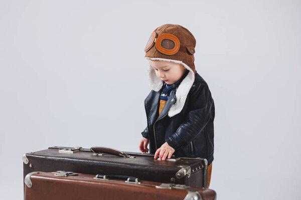 Happy little boy with a brown suitcase. Portrait of a child tourist, a child in overalls. Little traveler with a suitcase