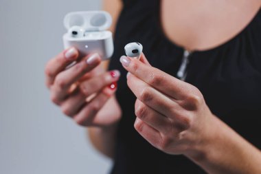 White wireless headphones in a woman's hand, close-up. Headset with charging case.