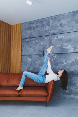 Klasik bej ayakkabılı, ince topuklu ve kot pantolonlu güzel ince kadın bacakları. Topuklu ayakkabılı şık kız kahverengi deri koltukta oturuyor.