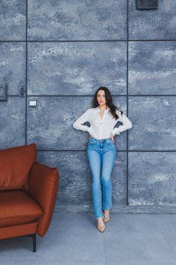 Klasik bej ayakkabılı, ince topuklu, kot pantolonlu ve beyaz gömlekli güzel, ince bir kadın. Yüksek topuklu şık bir kız güvenli bir şekilde yürüyor.