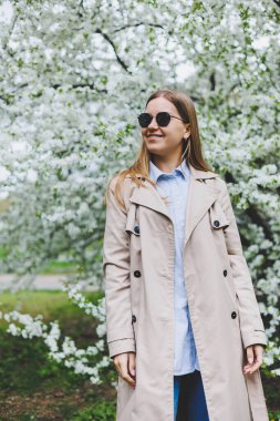 Şehir caddesinde akıllı telefon kullanarak yürüyen mutlu bir kadın. Güneş gözlüklü iş kadını dışarıda, ağacın altında cep telefonu kullanıyor. Kız mesaj yazıyor, sohbet ediyor, web sayfası kayıyor. Kameraya bakın.