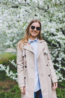 Şehir caddesinde akıllı telefon kullanarak yürüyen mutlu bir kadın. Güneş gözlüklü iş kadını dışarıda, ağacın altında cep telefonu kullanıyor. Kız mesaj yazıyor, sohbet ediyor, web sayfası kayıyor. Kameraya bakın.