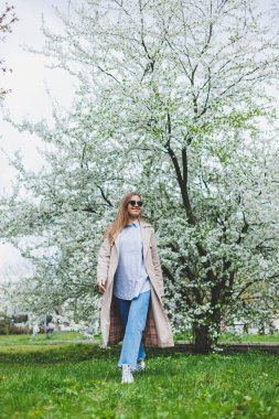Prag 'daki tepedeki tepede, doğal parktaki çiçek açan elma ağacının altında yürüyen arka plan kızı. Şapkalı ve kahverengi ceketli zarif genç bayan güneşli bahar gününde çiçek açan bahçenin tadını çıkarıyor..