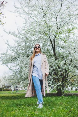 Prag 'daki tepedeki tepede, doğal parktaki çiçek açan elma ağacının altında yürüyen arka plan kızı. Şapkalı ve kahverengi ceketli zarif genç bayan güneşli bahar gününde çiçek açan bahçenin tadını çıkarıyor..