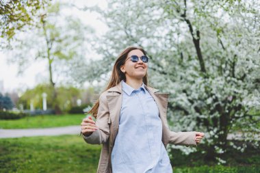 Prag 'daki tepedeki tepede, doğal parktaki çiçek açan elma ağacının altında yürüyen arka plan kızı. Şapkalı ve kahverengi ceketli zarif genç bayan güneşli bahar gününde çiçek açan bahçenin tadını çıkarıyor..
