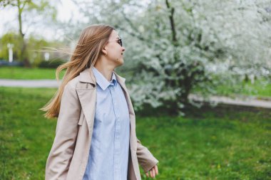 Prag 'daki tepedeki tepede, doğal parktaki çiçek açan elma ağacının altında yürüyen arka plan kızı. Şapkalı ve kahverengi ceketli zarif genç bayan güneşli bahar gününde çiçek açan bahçenin tadını çıkarıyor..