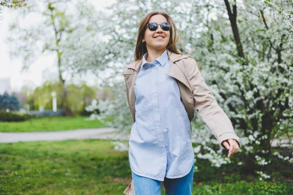 バックビューの女の子は プラハの丘の斜面にある自然公園で開花リンゴの木の下を歩く 帽子のエレガントな若い女性と日当たりの良い春の日に開花庭を楽しむ茶色のコート — ストック写真