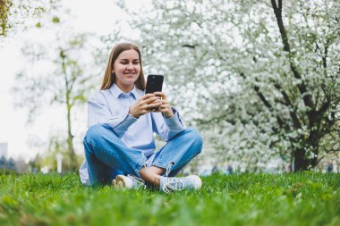 Şehir caddesinde akıllı telefon kullanarak yürüyen mutlu bir kadın. Güneş gözlüklü iş kadını dışarıda, ağacın altında cep telefonu kullanıyor. Kız mesaj yazıyor, sohbet ediyor, web sayfası kayıyor. Kameraya bakın.