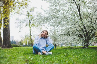 Şehir caddesinde akıllı telefon kullanarak yürüyen mutlu bir kadın. Güneş gözlüklü iş kadını dışarıda, ağacın altında cep telefonu kullanıyor. Kız mesaj yazıyor, sohbet ediyor, web sayfası kayıyor. Kameraya bakın.