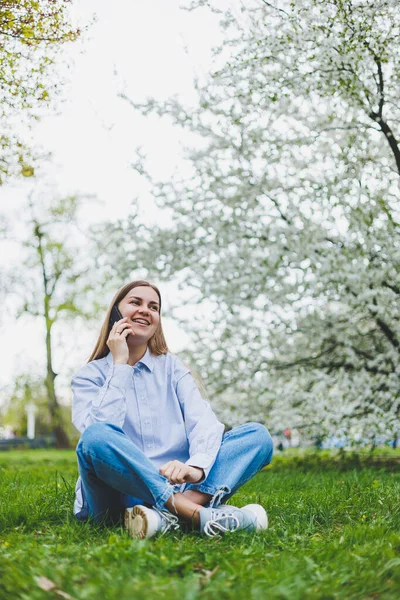 Şehir caddesinde akıllı telefon kullanarak yürüyen mutlu bir kadın. Güneş gözlüklü iş kadını dışarıda, ağacın altında cep telefonu kullanıyor. Kız mesaj yazıyor, sohbet ediyor, web sayfası kayıyor. Kameraya bakın.