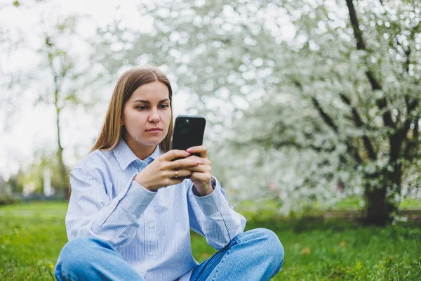 Şehir caddesinde akıllı telefon kullanarak yürüyen mutlu bir kadın. Güneş gözlüklü iş kadını dışarıda, ağacın altında cep telefonu kullanıyor. Kız mesaj yazıyor, sohbet ediyor, web sayfası kayıyor. Kameraya bakın.