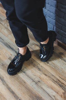 Beautiful woman with legs in fashionable clothes, stylish leather black patent leather lace-up shoes close-up. Womens image in spring style