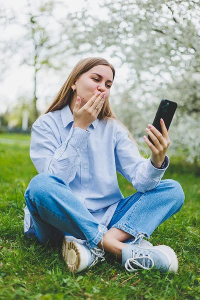 Şehir caddesinde akıllı telefon kullanarak yürüyen mutlu bir kadın. Güneş gözlüklü iş kadını dışarıda, ağacın altında cep telefonu kullanıyor. Kız mesaj yazıyor, sohbet ediyor, web sayfası kayıyor. Kameraya bakın.