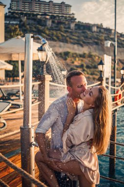 Deniz kenarında mutlu bir çift. Bir adam ve bir kız açık hava rıhtımında duşun altındalar. Tatildeki mutlu çift. Deniz kenarındaki kadın ve erkek.