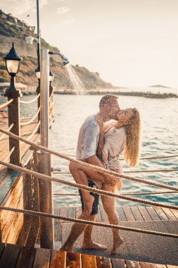Deniz kenarında mutlu bir çift. Bir adam ve bir kız açık hava rıhtımında duşun altındalar. Tatildeki mutlu çift. Deniz kenarındaki kadın ve erkek.