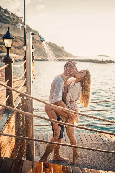 Deniz kenarında mutlu bir çift. Bir adam ve bir kız açık hava rıhtımında duşun altındalar. Tatildeki mutlu çift. Deniz kenarındaki kadın ve erkek.