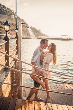 Deniz kenarında mutlu bir çift. Bir adam ve bir kız açık hava rıhtımında duşun altındalar. Tatildeki mutlu çift. Deniz kenarındaki kadın ve erkek.
