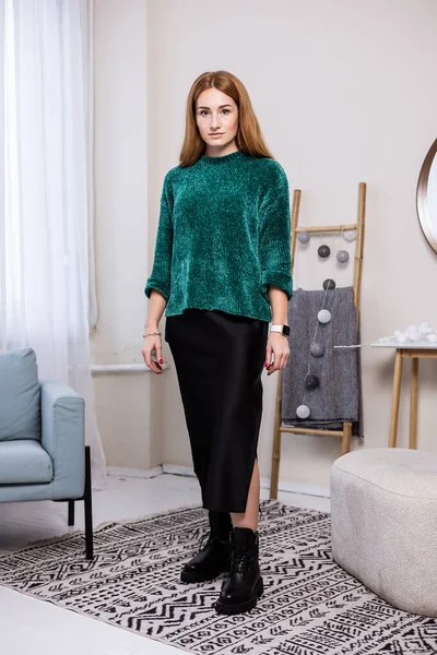 Yeşil, sıcak bir kazak ve siyah deri çizmeli siyah etekli bir kadın. Şık bir sonbahar kıyafeti..