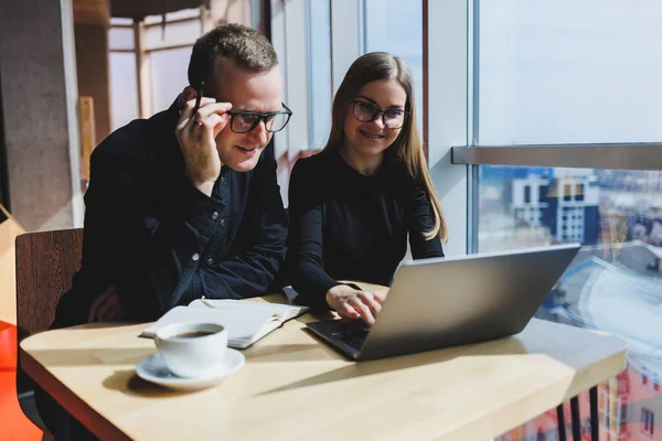 Gülümseyen genç erkek ve kadın yönetici masada oturuyor, bilgisayar ekranına bakıyor, girişimci yazılımları açıklıyor ya da iş arkadaşlarıyla online proje üzerinde çalışıyor..