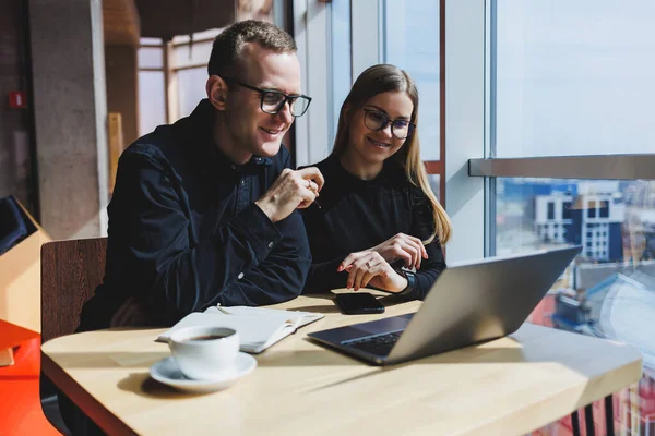 Gülümseyen genç erkek ve kadın yönetici masada oturuyor, bilgisayar ekranına bakıyor, girişimci yazılımları açıklıyor ya da iş arkadaşlarıyla online proje üzerinde çalışıyor..