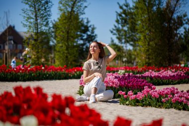 Yazlık elbiseli ve şapkalı, güneşli bir günde çayırda açan lalelerin yanında yürüyen kimliği belirsiz bir kadının arka planı.