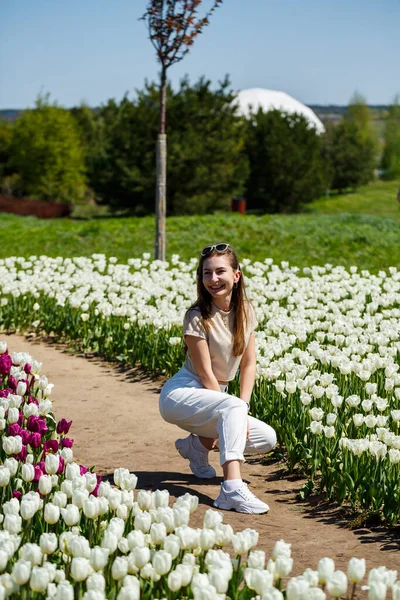 Laughing woman turns and looks to the camera walking between tulips and picnic tables