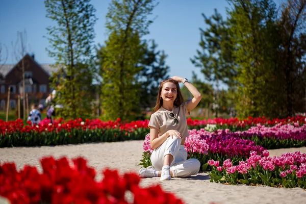Yazlık elbiseli ve şapkalı, güneşli bir günde çayırda açan lalelerin yanında yürüyen kimliği belirsiz bir kadının arka planı.