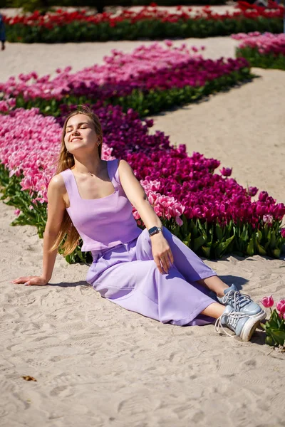 Yazlık elbiseli ve şapkalı, güneşli bir günde çayırda açan lalelerin yanında yürüyen kimliği belirsiz bir kadının arka planı.