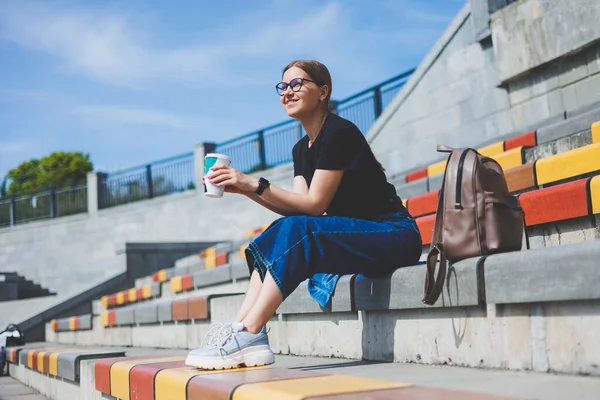 Kadın merdivenlerde oturuyor ve elinde tek kullanımlık bir fincan kahve tutuyor..