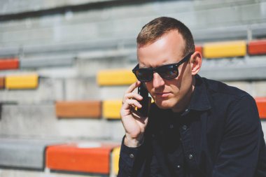 Şehirdeki şehir merkezinde dinlenirken gülümseyen modaya uygun giyinmiş neşeli hippi adam boş zamanlarında cep telefonu kullanıyor. Güneş gözlüklü mutlu Orta Doğulu erkek blogcu seyahat yaşam tarzının keyfini çıkarıyor.