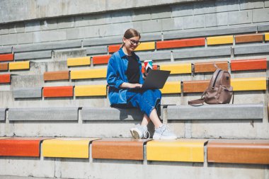 Görüntü açık bej duvara Yürüyüş ve gümüş laptop ve paket servisi olan restoran elinde kahve ile geriye doğru seyir neşeli esmer kadın