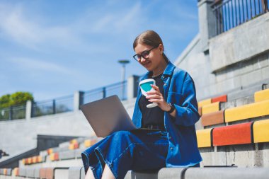 Görüntü açık bej duvara Yürüyüş ve gümüş laptop ve paket servisi olan restoran elinde kahve ile geriye doğru seyir neşeli esmer kadın