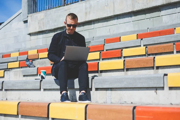 Genç işadamı ofisinin önündeki bankta otururken bilgisayarla çalışıyor.