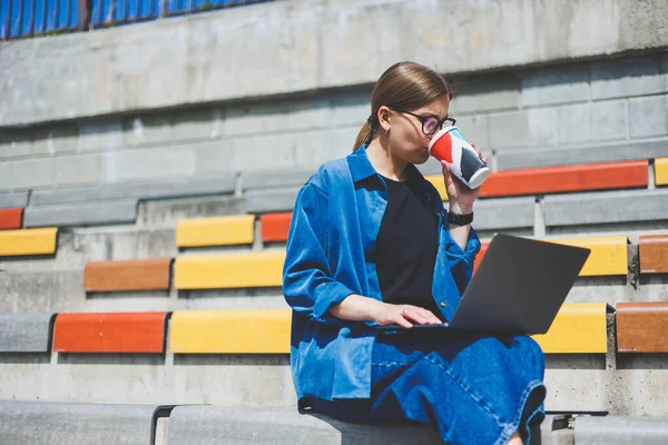 Görüntü açık bej duvara Yürüyüş ve gümüş laptop ve paket servisi olan restoran elinde kahve ile geriye doğru seyir neşeli esmer kadın
