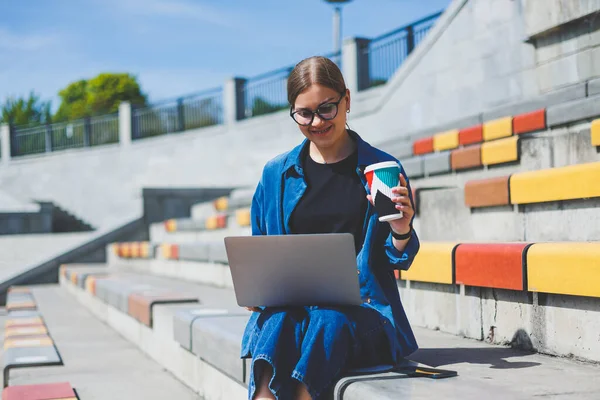 Görüntü açık bej duvara Yürüyüş ve gümüş laptop ve paket servisi olan restoran elinde kahve ile geriye doğru seyir neşeli esmer kadın