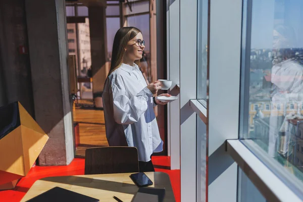 Attractive female blogger holding a modern smartphone gadget in her hands, looking thoughtful and daydreaming, a young european blogger holding a mobile phone, ponders an idea for a social media post