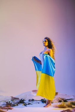 Güzel, mutlu, neşeli, düz saçlı bir kızın el ele yürümesi eğlenceli. Açık gri pastel arka planda izole edilmiş Ukrayna bayrağı.