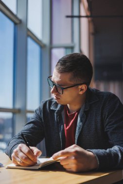 Modern bir dizüstü bilgisayarla uzaktan çalışan, mola sırasında masaya oturup kameraya gülümseyen, vizyon düzeltme gözlüklü mutlu bir insan programcı portresi.