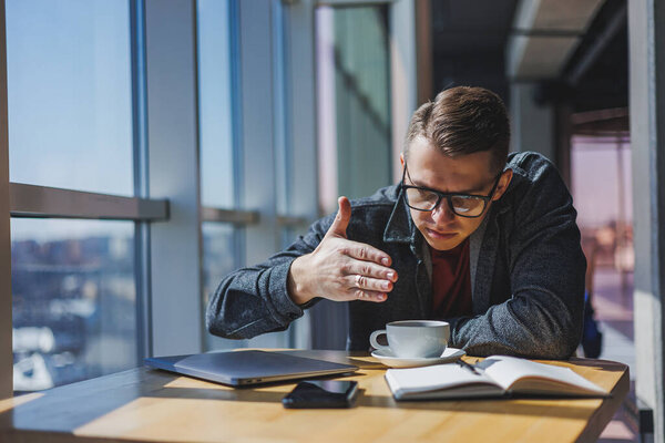 Portrait of a man, IT professional, working remotely with a modern laptop, sitting at a table and smiling at the camera during a break, a happy human programmer in vision correction glasses