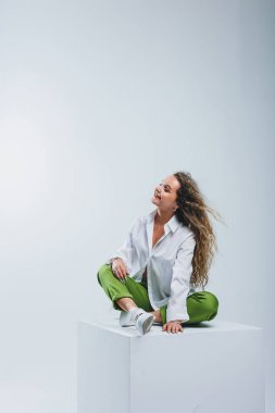 Beyaz pamuklu gömlekli kıvırcık saçlı ve beyaz izole edilmiş pantolonlu pozitif bir kadın. Kadın kıyafetleri..