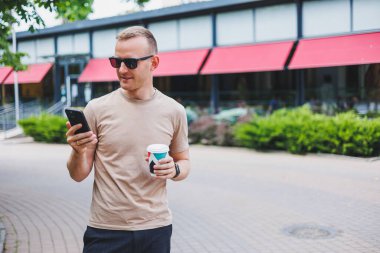 Sakallı, gülümseyen, beyaz gömlekli ve güneş gözlüklü şık bir adam şehrin sokaklarında duruyor ve cep telefonundan arıyor..