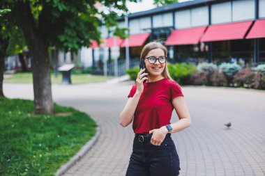 Gri kazaklı, mavi kotlu ve gözlüklü genç bir bayan kaldırımda duruyor. New York 'ta alışveriş torbaları taşıyor ve akıllı telefondan mesajlaşıyor.
