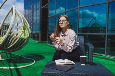 Not defteriyle sokak kafesinde poz veren neşeli bayan öğrenci ders kitabı ve kahve bardağıyla dışarıda gülümseyen başarılı kadın.