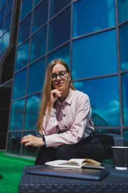 Not defteriyle sokak kafesinde poz veren neşeli bayan öğrenci ders kitabı ve kahve bardağıyla dışarıda gülümseyen başarılı kadın.