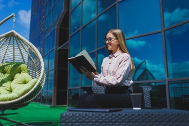 Not defteriyle sokak kafesinde poz veren neşeli bayan öğrenci ders kitabı ve kahve bardağıyla dışarıda gülümseyen başarılı kadın.