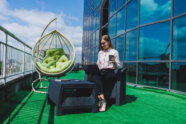 İş akışı için dizüstü bilgisayarı olan neşeli bir serbest çalışan sokak kafesinde poz veren, bilgisayar ve kahve bardağıyla gülümseyen başarılı bir kadın.