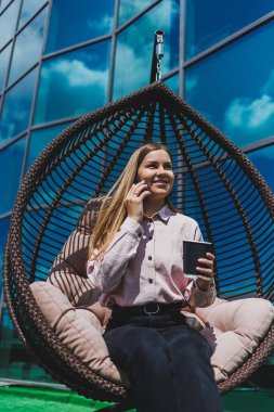 Güneşli bir günde açık havada kahve molası veren gözlüklü neşeli bir iş kadınının portresi. Ofisin arka planında otururken telefonda konuşan başarılı bir kadın yönetici.