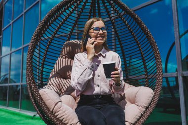 Güneşli bir günde açık havada kahve molası veren gözlüklü neşeli bir iş kadınının portresi. Ofisin arka planında otururken telefonda konuşan başarılı bir kadın yönetici.