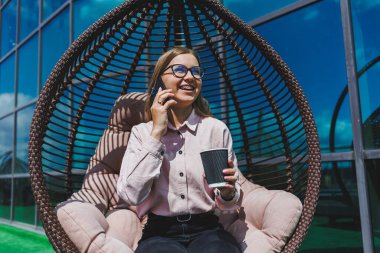 Güneşli bir günde açık havada kahve molası veren gözlüklü neşeli bir iş kadınının portresi. Ofisin arka planında otururken telefonda konuşan başarılı bir kadın yönetici.